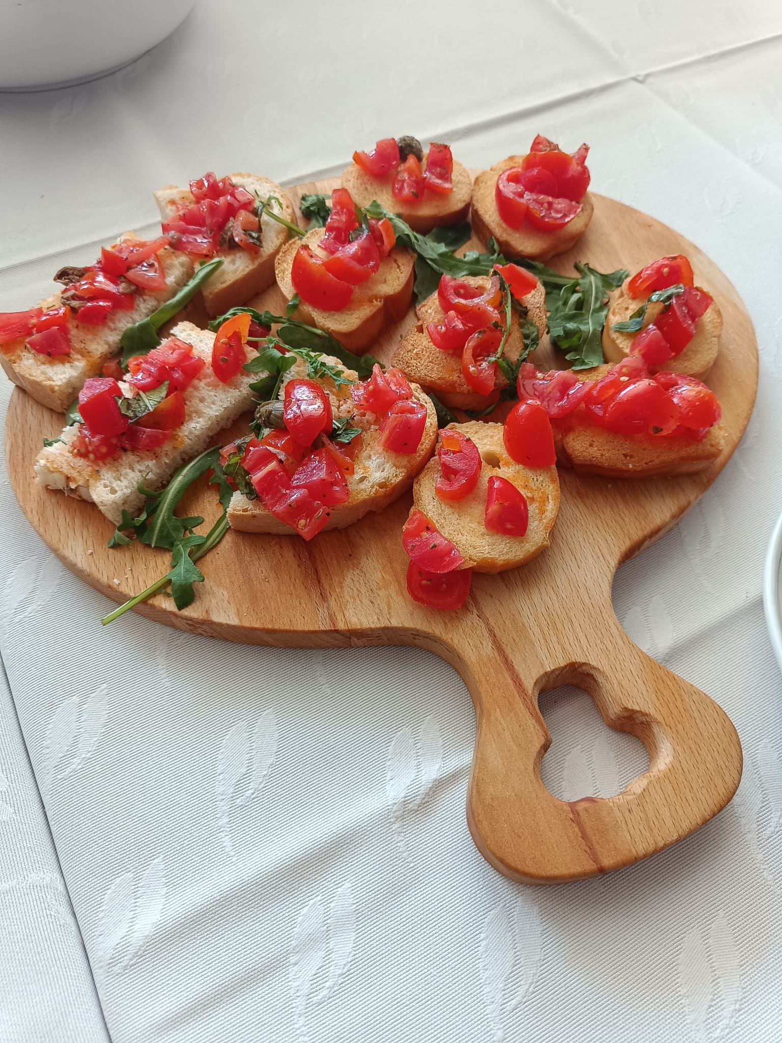 Crostini con pomodorini freschi, rucola e capperi su tagliere a forma di cuore